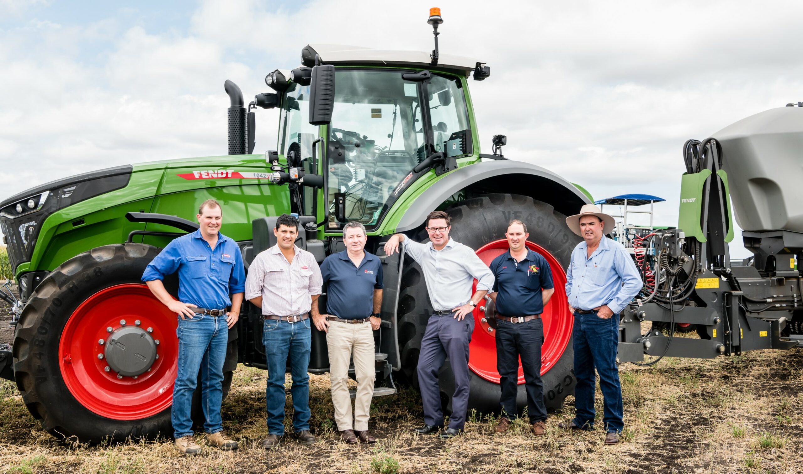 Six men standing in front of a green tractor
