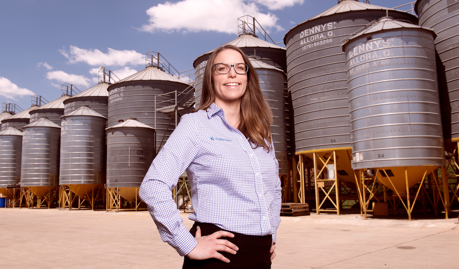 Woman wearing Pacific Seeds branded shirt standing in front of silos